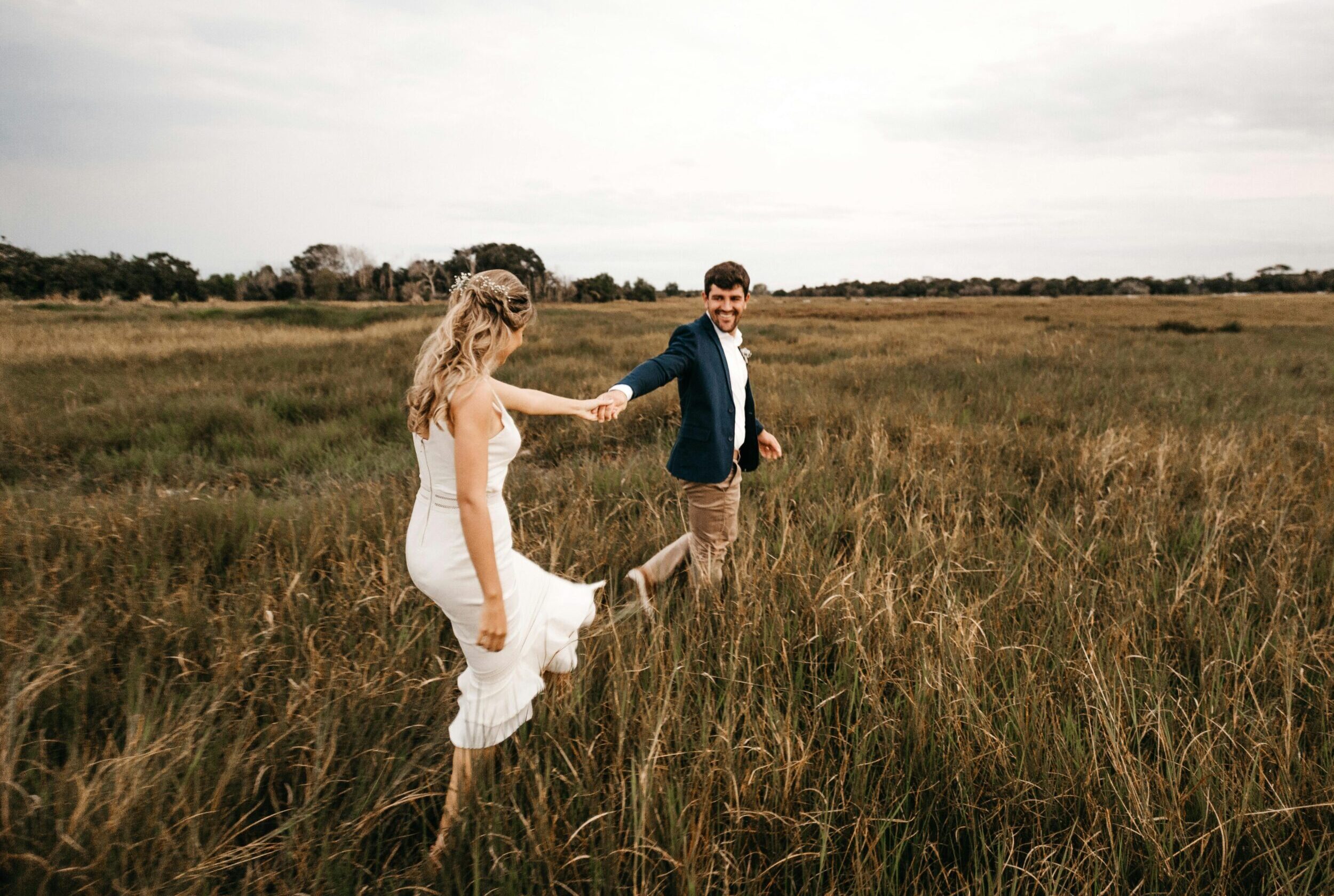 Happy couple holding hands and walking through a grassy field, embracing love and freedom.